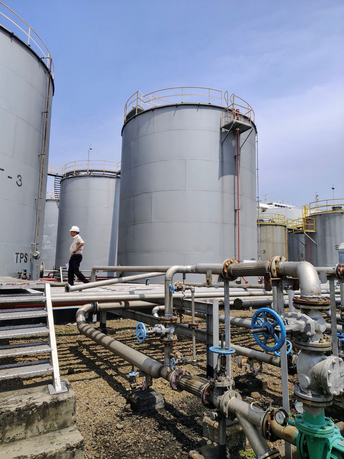 An operator walking beside bulk liquid storage tanks and pipelines at the terminal